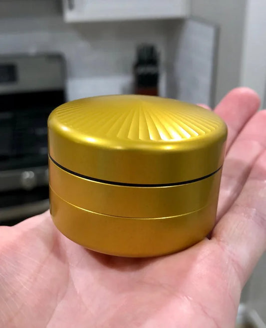 gold pucc herb grinder sitting on person's hand